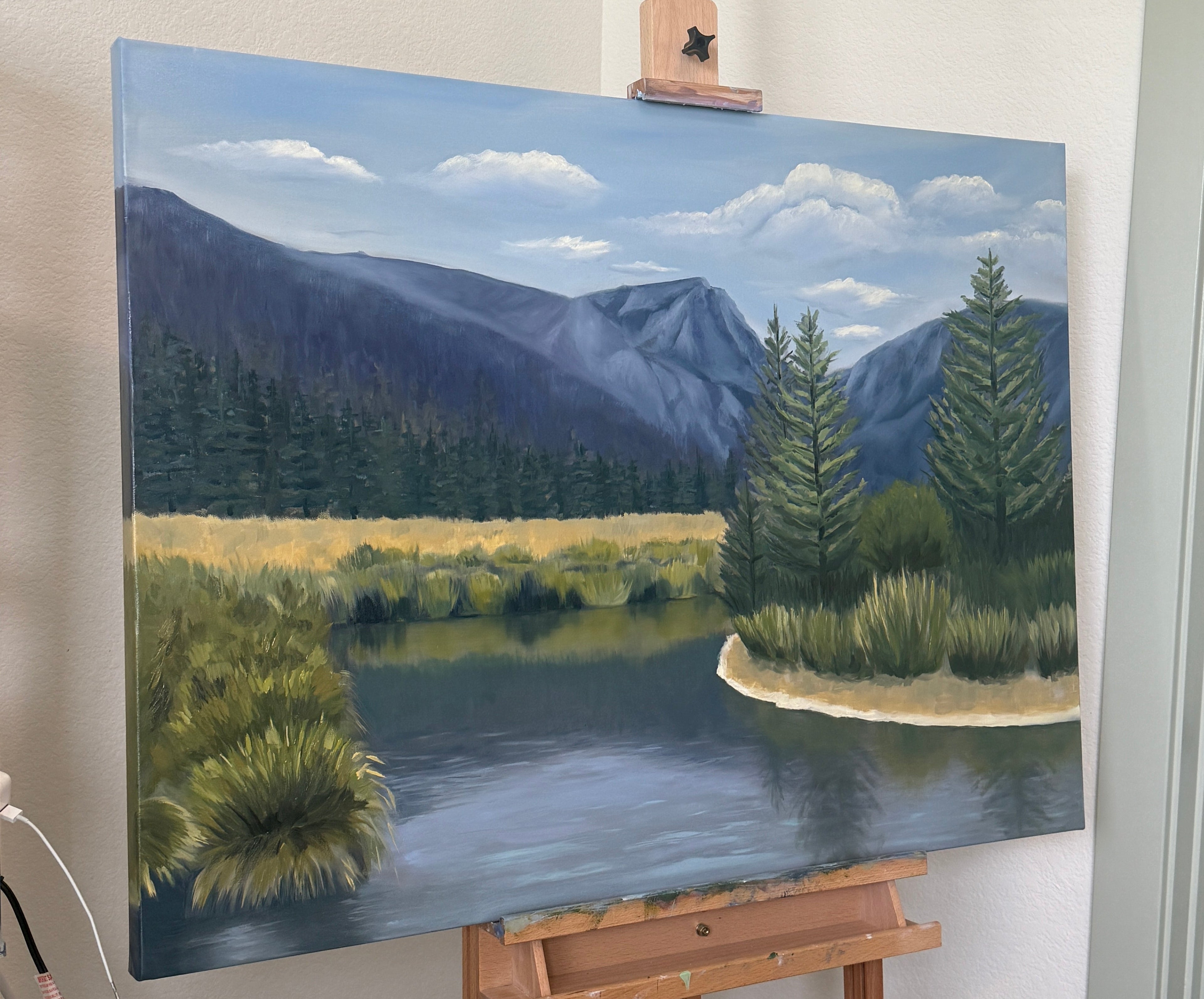 Painting of a landscape with trees and mountains on an easel.